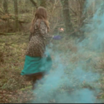 Jess in the woods with a blue smoke bomb